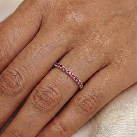 Close-up of a hand wearing a pink gemstone ring on a neutral background