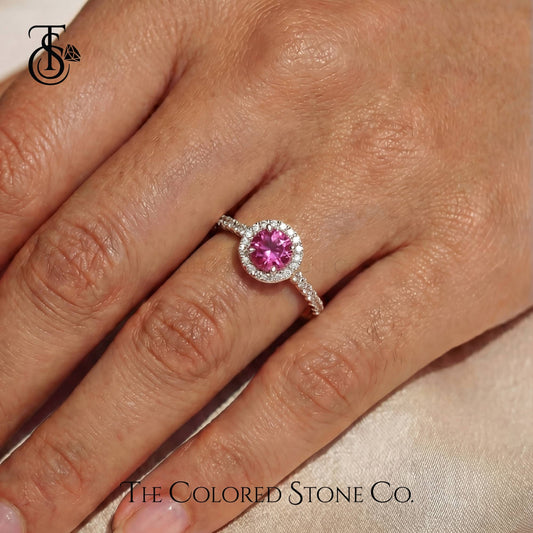 Ring with a pink gemstone on a hand, branded 'The Colored Stone Co'.