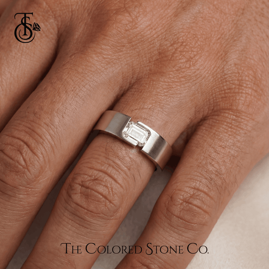 Silver men's wedding ring with a diamond on a person's finger, branded 'The Colored Stone Co'.