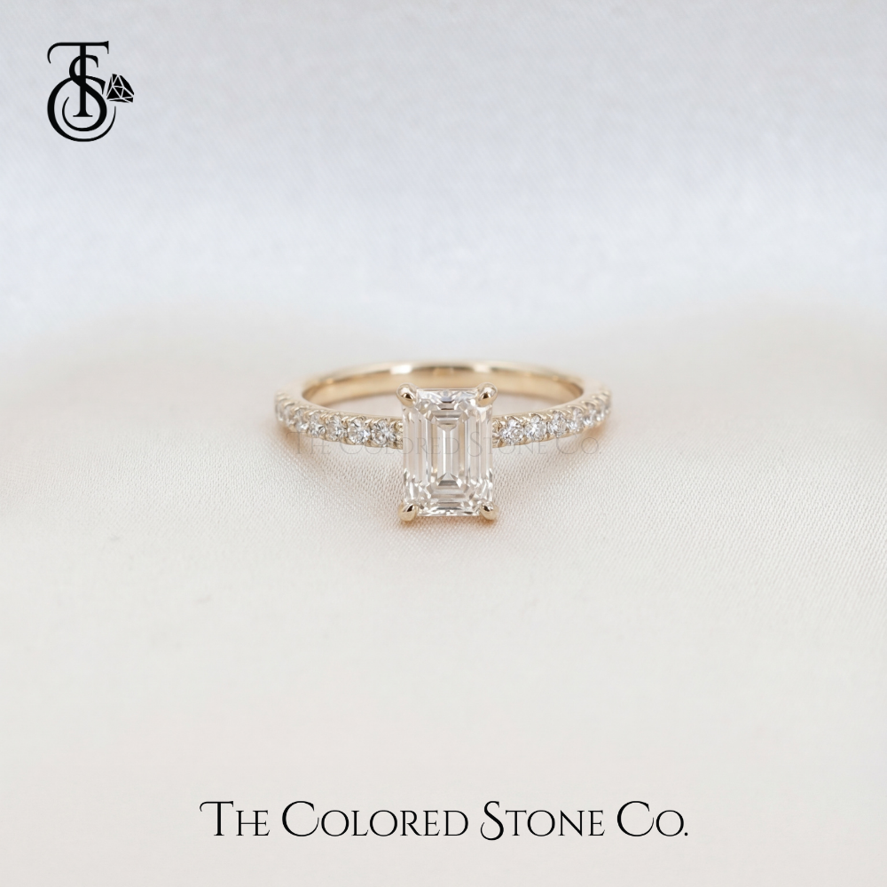 Yellow gold Diamond engagement ring with emerald-cut diamond on a light background, featuring 'The Colored Stone Co.' branding.