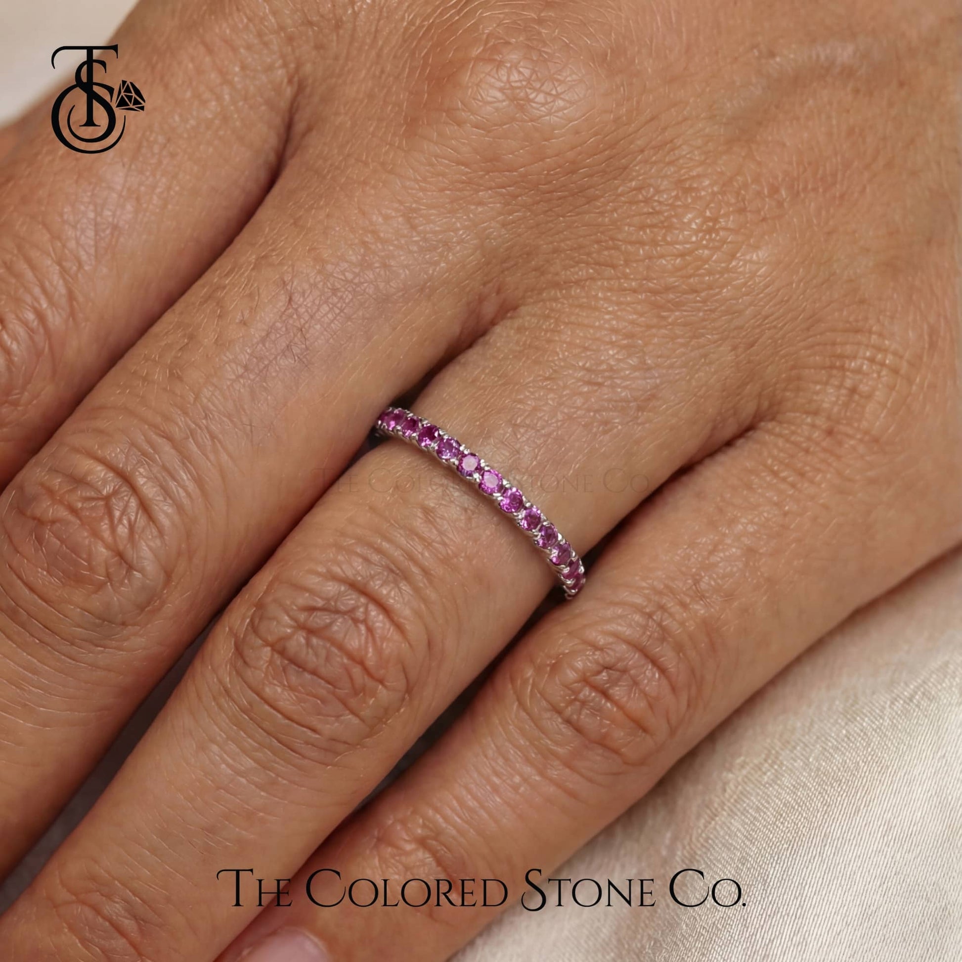 Close-up of a hand wearing a pink gemstone ring with 'The Colored Stone Co.' branding.