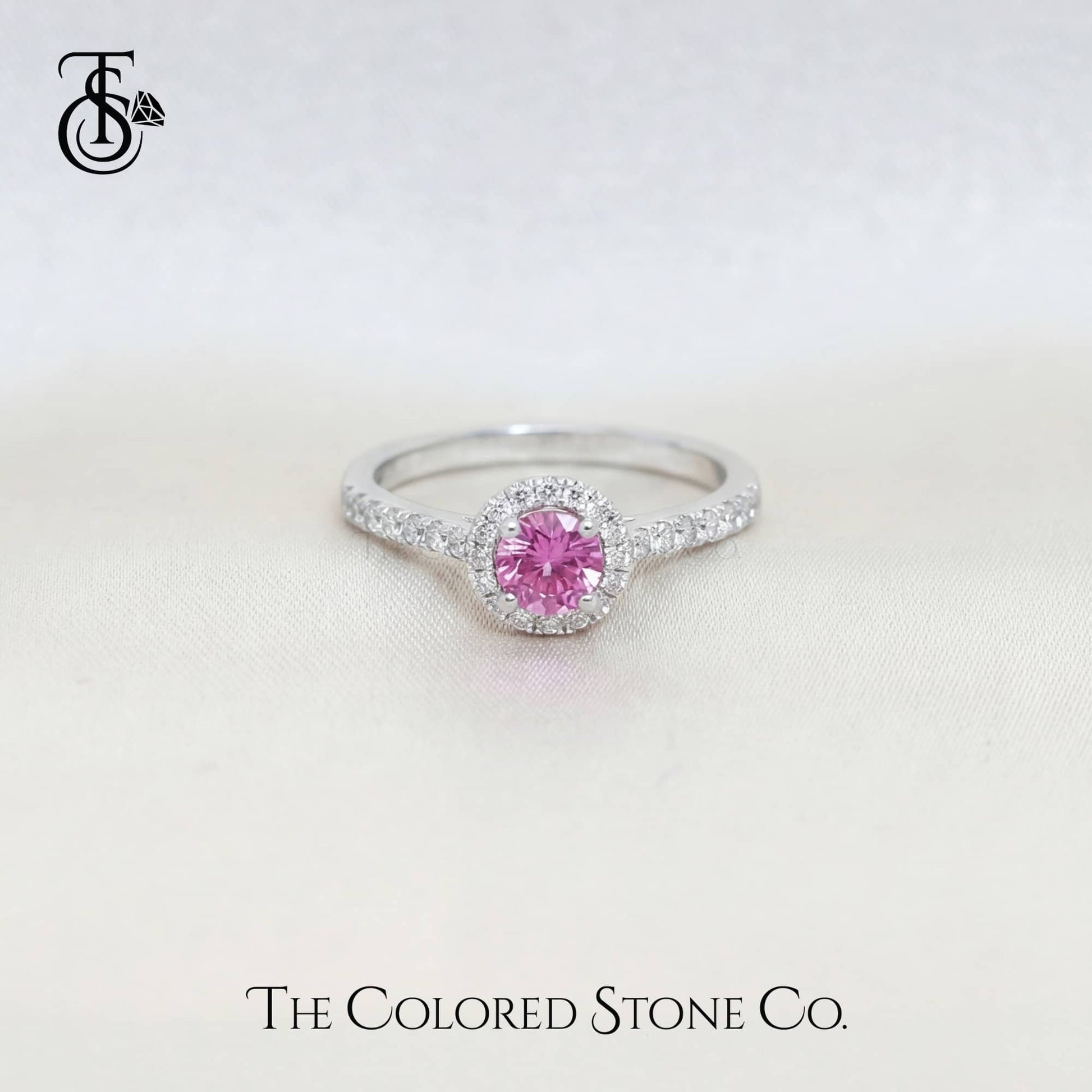 white gold engagement ring with a pink sapphire gemstone on a light background, branded 'The Colored Stone Co'.