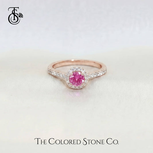 Rose gold engagement ring with a pink sapphire gemstone on a light background, branded 'The Colored Stone Co'.