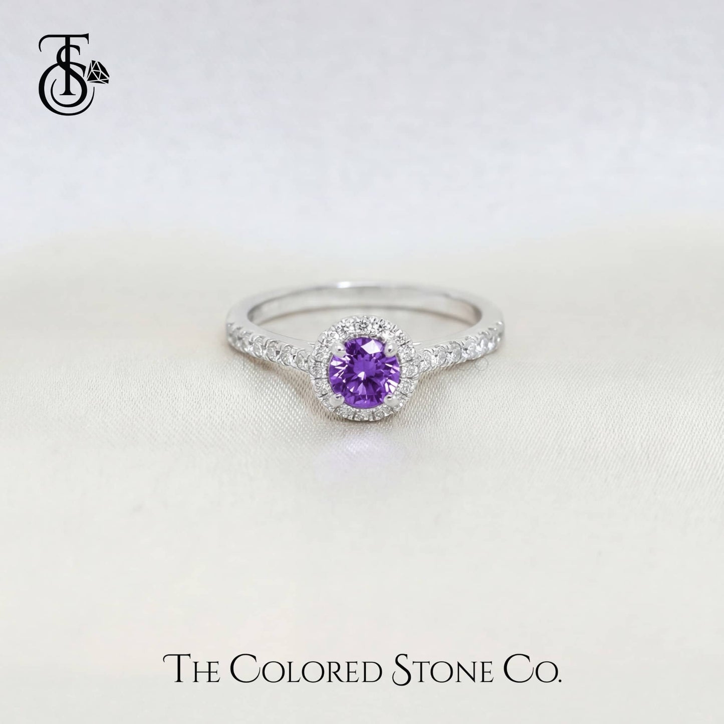 white gold engagement ring with a purple sapphire gemstone on a white background, featuring The Colored Stone Co. branding.