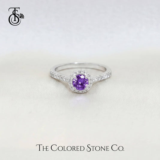 white gold engagement ring with a purple sapphire gemstone on a white background, featuring The Colored Stone Co. branding.