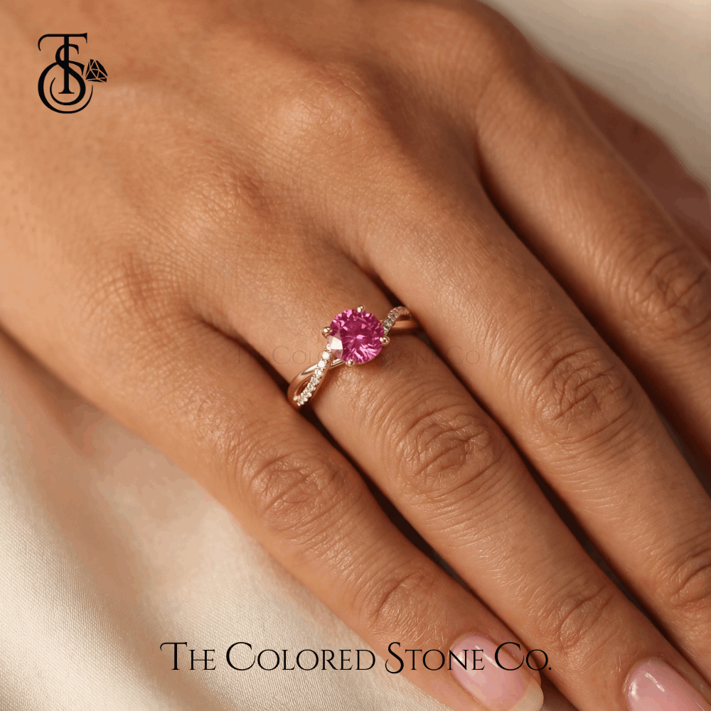 Engagement Ring with a pink sapphhire gemstone on a hand, featuring 'The Colored Stone Co' branding.
