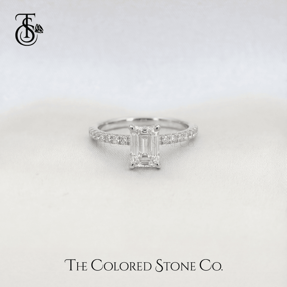 white gold Diamond engagement ring with emerald-cut stone on a light gray background, featuring The Colored Stone Co. branding.