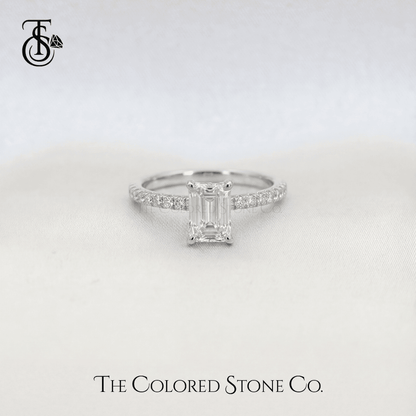white gold Diamond engagement ring with emerald-cut stone on a light gray background, featuring The Colored Stone Co. branding.