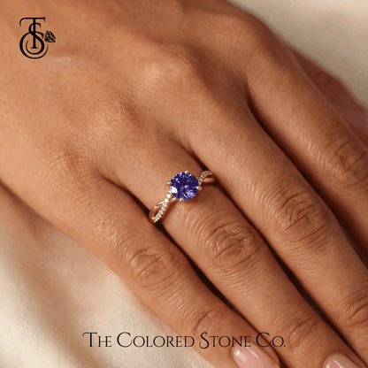 Engagement Ring with a purple sapphire gemstone on a hand, branded 'The Colored Stone Co'.