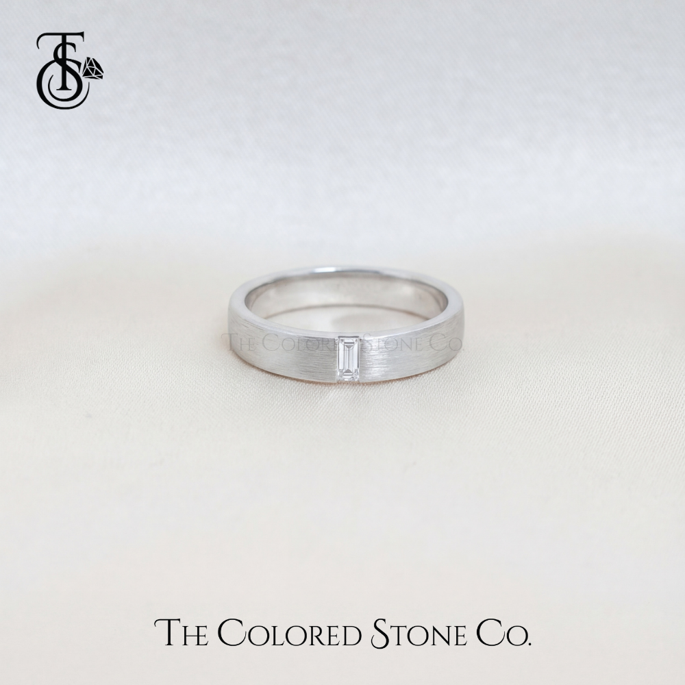 Silver men's wedding ring with a baguette cut diamond on a light gray background, featuring 'The Colored Stone Co.' branding.