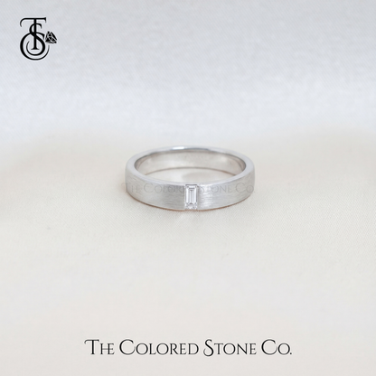 Silver men's wedding ring with a baguette cut diamond on a light gray background, featuring 'The Colored Stone Co.' branding.