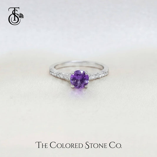 white gold engagement ring with a purple sapphire gemstone on a light background, branded 'The Colored Stone Co'.