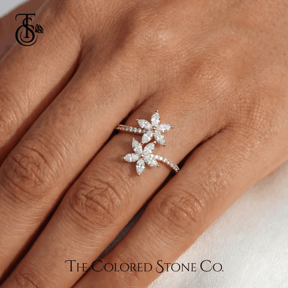 Floral diamond ring on a hand with 'The Colored Stone Co.' branding.