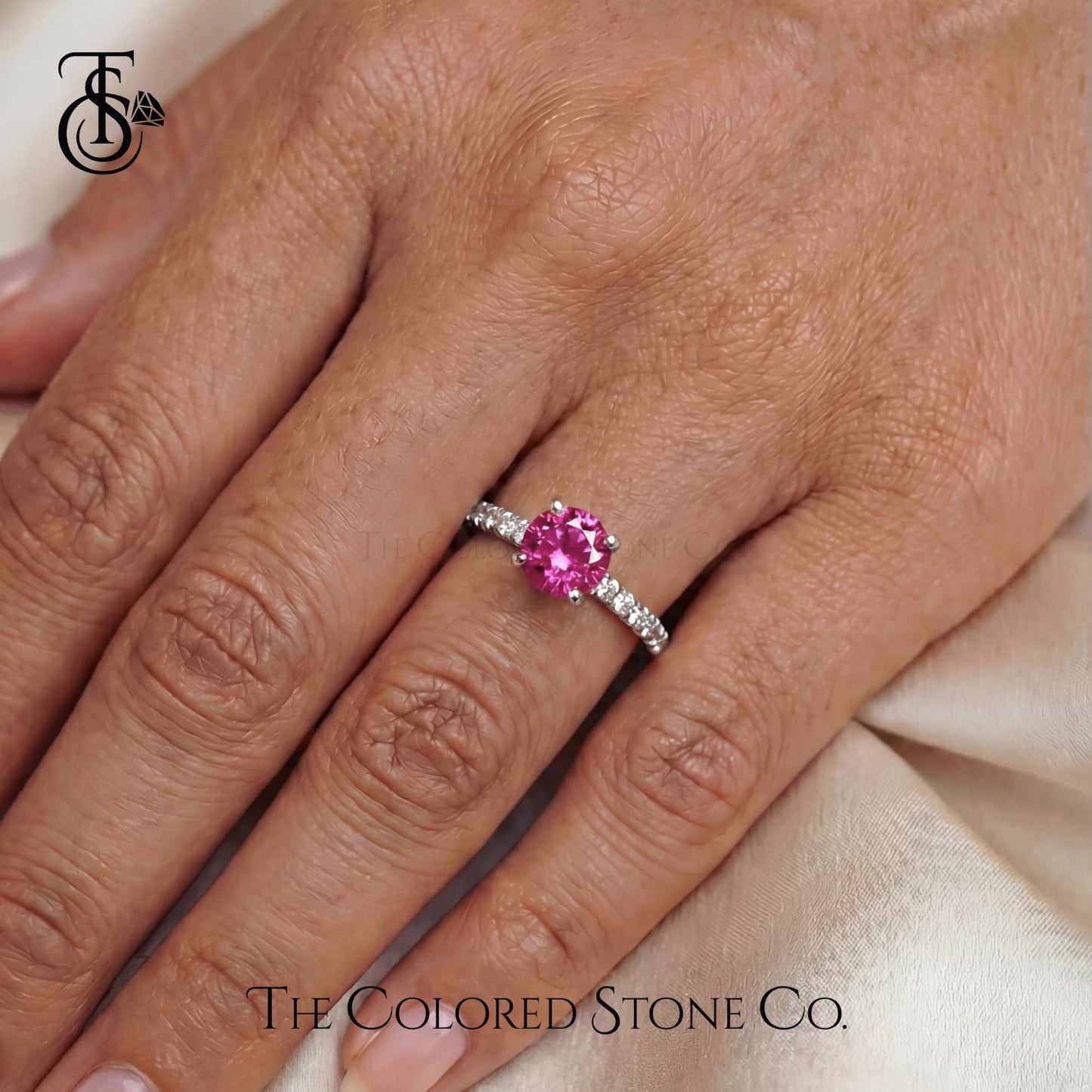 Ring with a pink gemstone on a hand, featuring 'The Colored Stone Co.' branding.