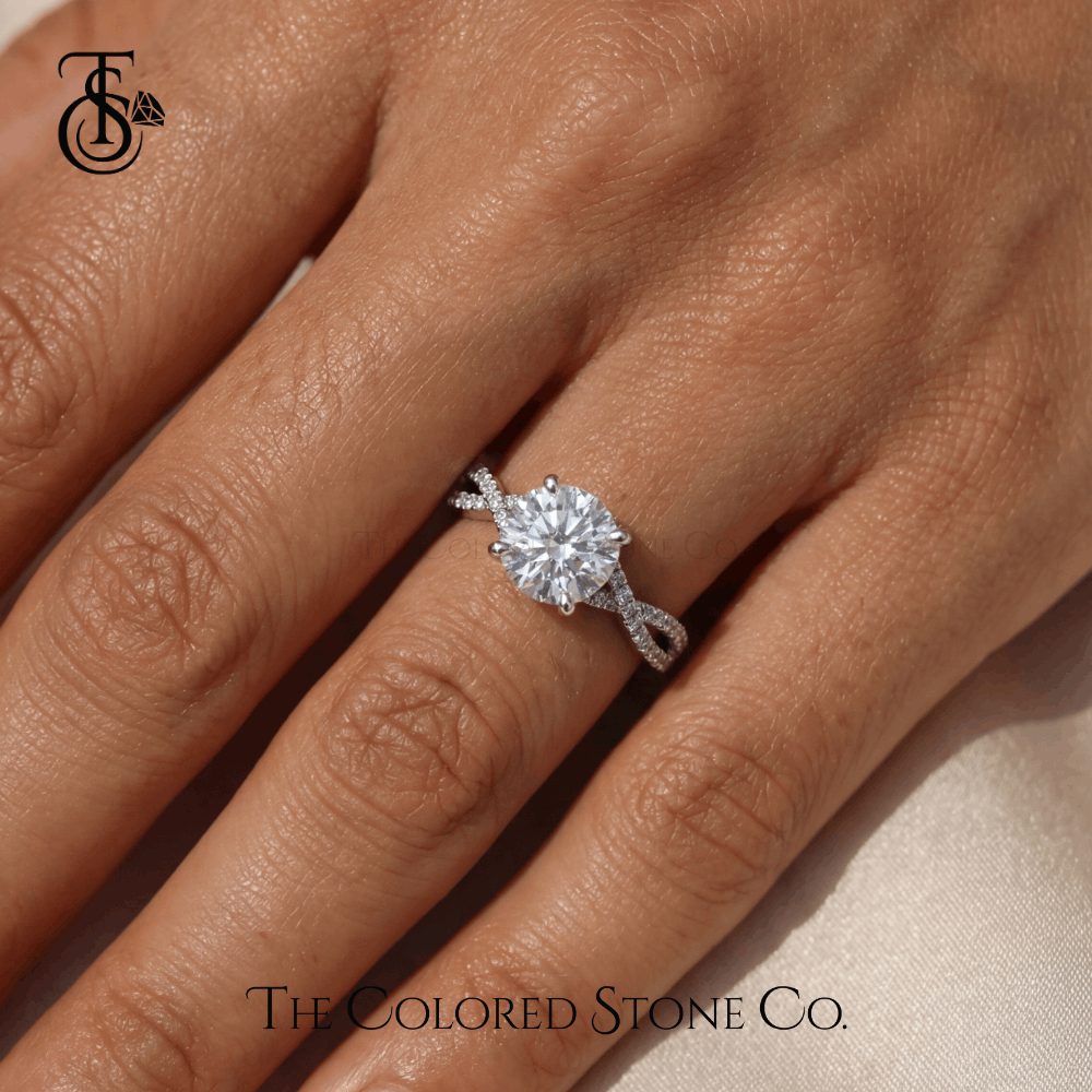 Diamond engagement ring on a finger with 'The Colored Stone Co.' branding.