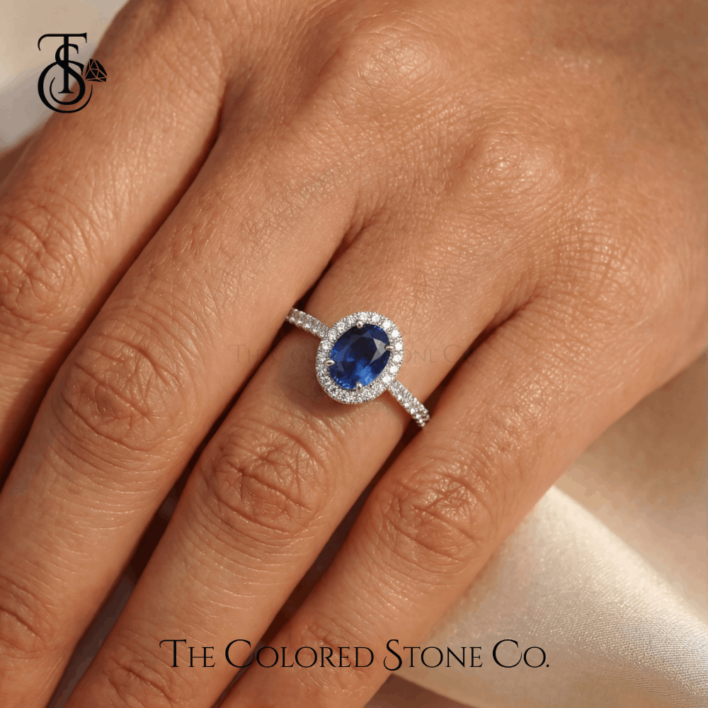 Engagement Ring with blue gemstone on a hand, featuring 'The Colored Stone Co.' logo.