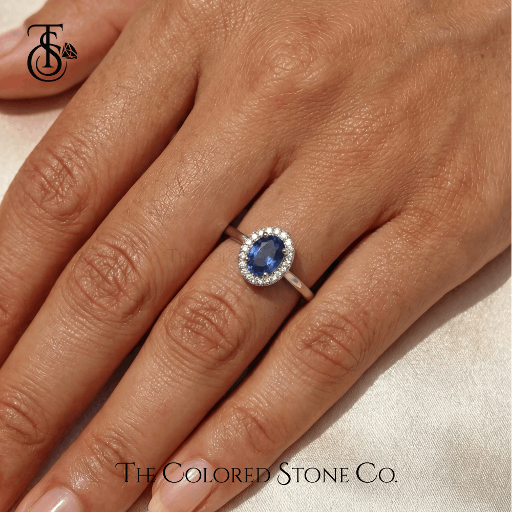 Engagement Ring with a blue sapphire gemstone on a hand, featuring The Colored Stone Co. logo.