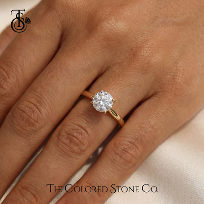 Yellow Gold engagement ring with a diamond on a hand, branded 'The Colored Stone Co'.
