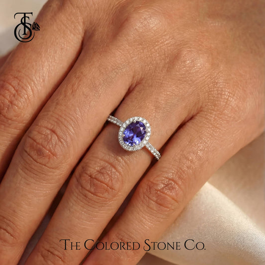 Ring with a purple gemstone on a hand, branded 'The Colored Stone Co'.