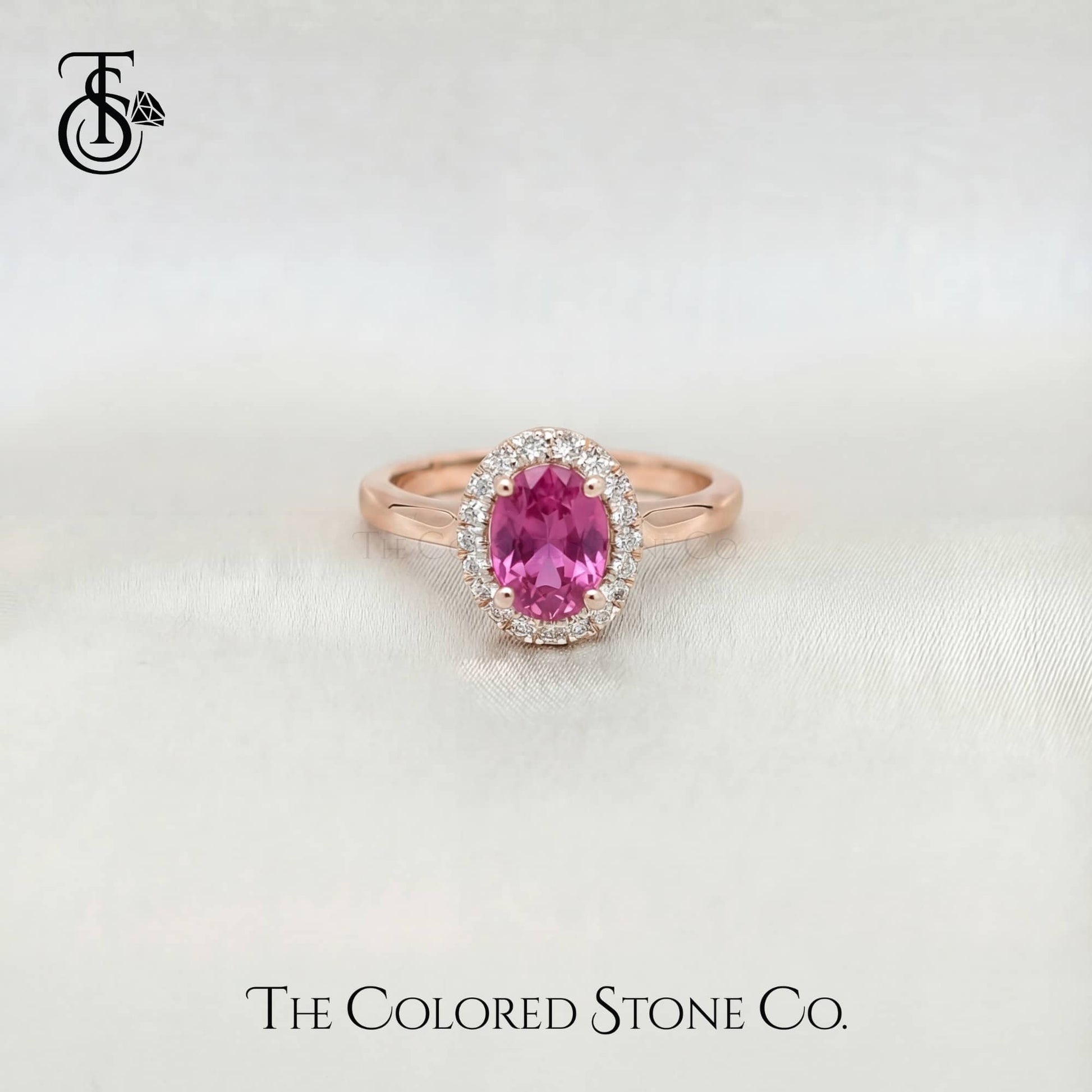 Rose gold engagement ring with a pink sapphire gemstone on a light background, featuring 'The Colored Stone Co.' branding.