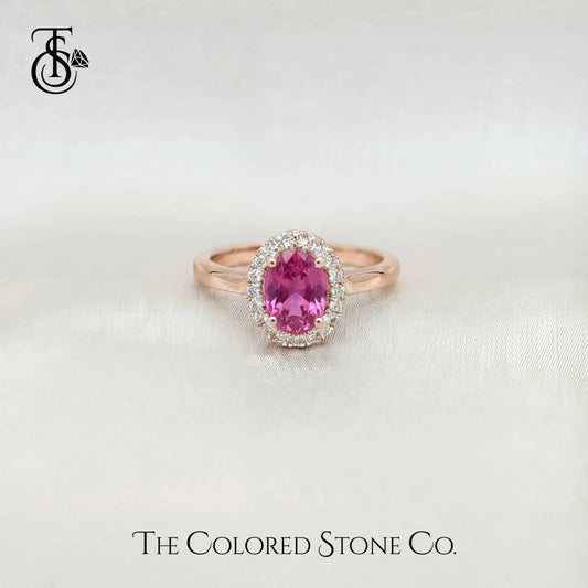 Rose gold engagement ring with a pink sapphire gemstone on a light background, featuring 'The Colored Stone Co.' branding.