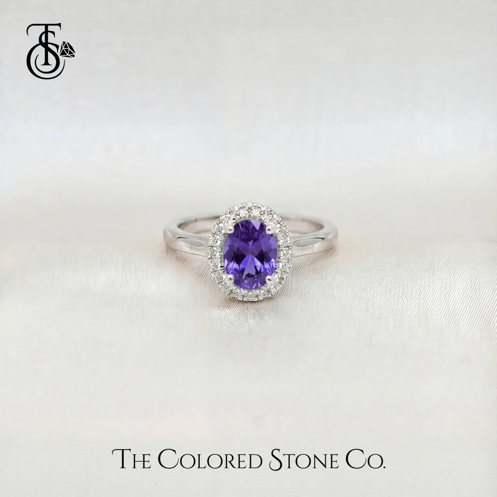 white gold engagement ring with a purple sapphire gemstone on a white background, branded 'The Colored Stone Co'.