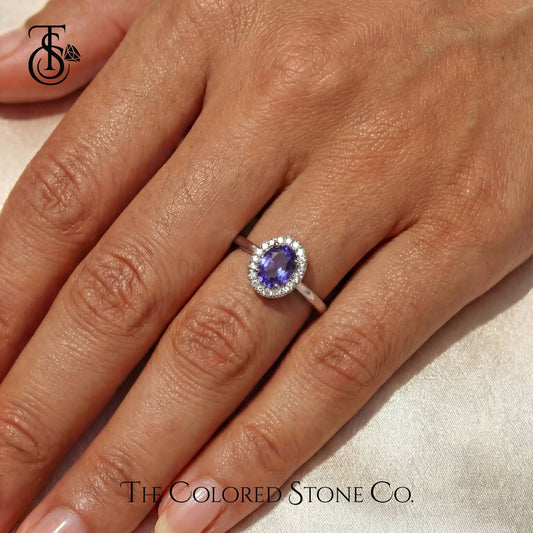 Ring with a purple sapphire gemstone on a hand, branded 'The Colored Stone Co'.