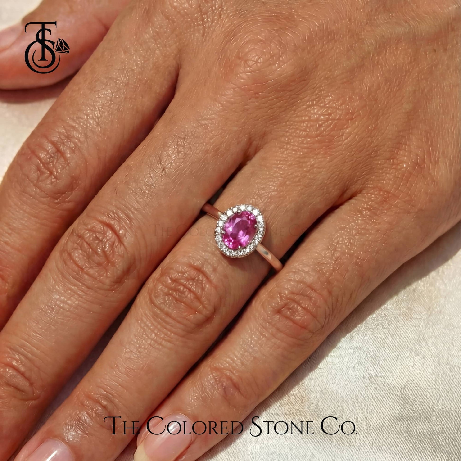 Pink gemstone ring on a hand with 'The Colored Stone Co.' branding.
