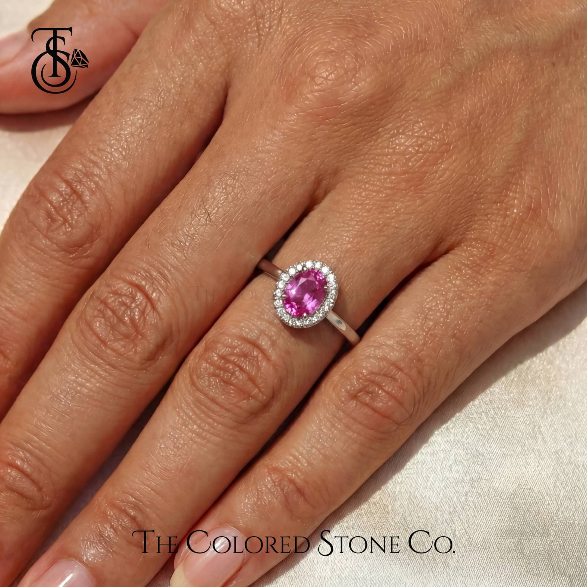 Pink gemstone ring on a hand with 'The Colored Stone Co.' branding.