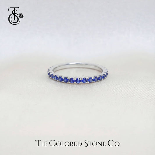 white gold wedding ring with blue stones on a white background, branded 'The Colored Stone Co'.