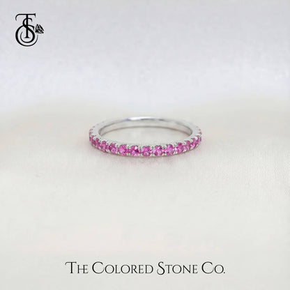 white gold wedding ring with pink stones on a white background, branded 'The Colored Stone Co'.