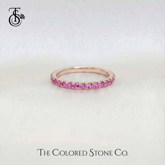 Rose gold wedding ring with pink gemstones on a light gray background, branded 'The Colored Stone Co'.