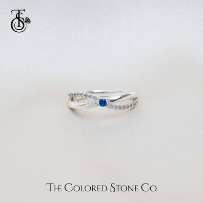 Silver ring with a blue gemstone on a light gray background, featuring 'The Colored Stone Co.' branding.