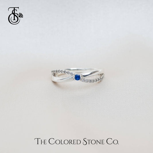 Silver ring with a blue gemstone on a light gray background, featuring 'The Colored Stone Co.' branding.