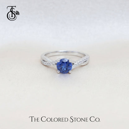 white gold engagement ring with a blue sapphire gemstone on a light background, featuring 'The Colored Stone Co.' branding.