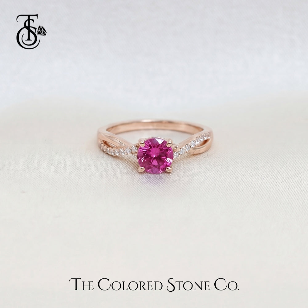 Rose gold engagement ring with a pink sapphire gemstone on a light background, featuring 'The Colored Stone Co.' branding.