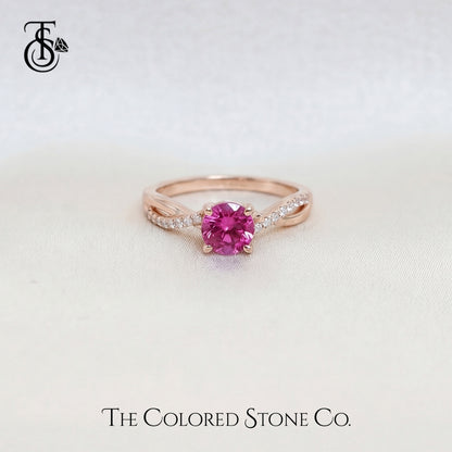 Rose gold engagement ring with a pink sapphire gemstone on a light background, featuring 'The Colored Stone Co.' branding.