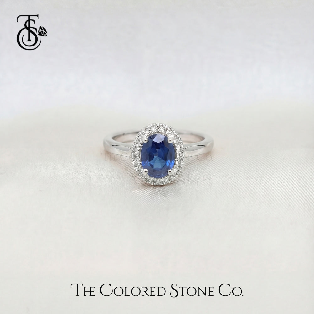 white gold engagement ring with a blue sapphire gemstone on a white background, branded 'The Colored Stone Co'.