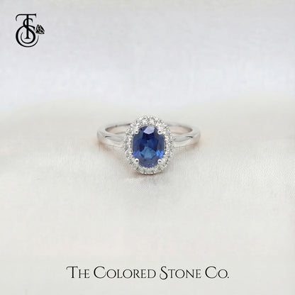 white gold engagement ring with a blue sapphire gemstone on a white background, branded 'The Colored Stone Co'.