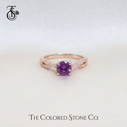 Rose gold engagement ring with a purple sapphire gemstone on a light gray background, featuring 'The Colored Stone Co.' branding.
