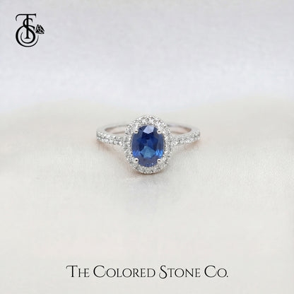 white gold engagement ring with a blue sapphire gemstone on a white background, branded 'The Colored Stone Co'.
