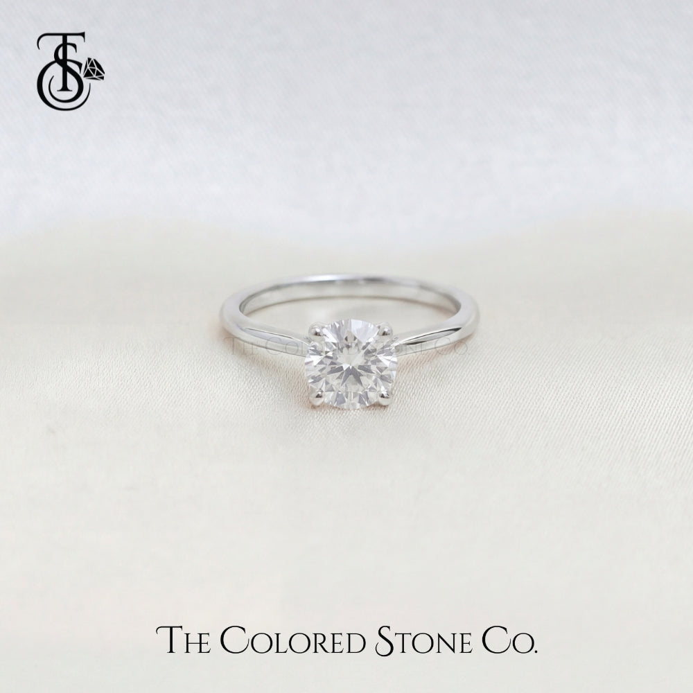 White Gold engagement ring with a diamond on a light background, featuring The Colored Stone Co. branding.