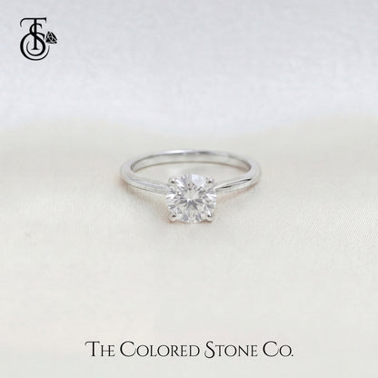 White Gold engagement ring with a diamond on a light background, featuring The Colored Stone Co. branding.